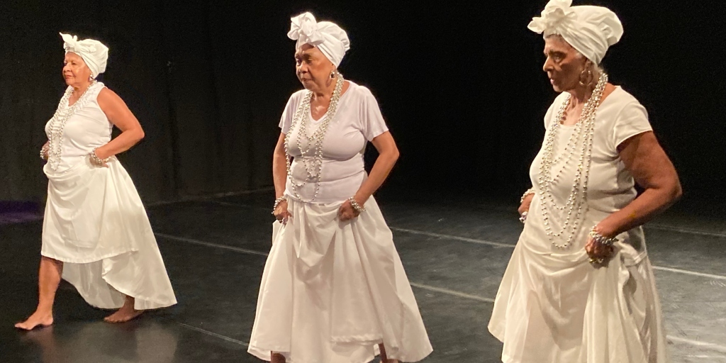 No palco, três baianas de escola de samba apresentam performatividade ritmada