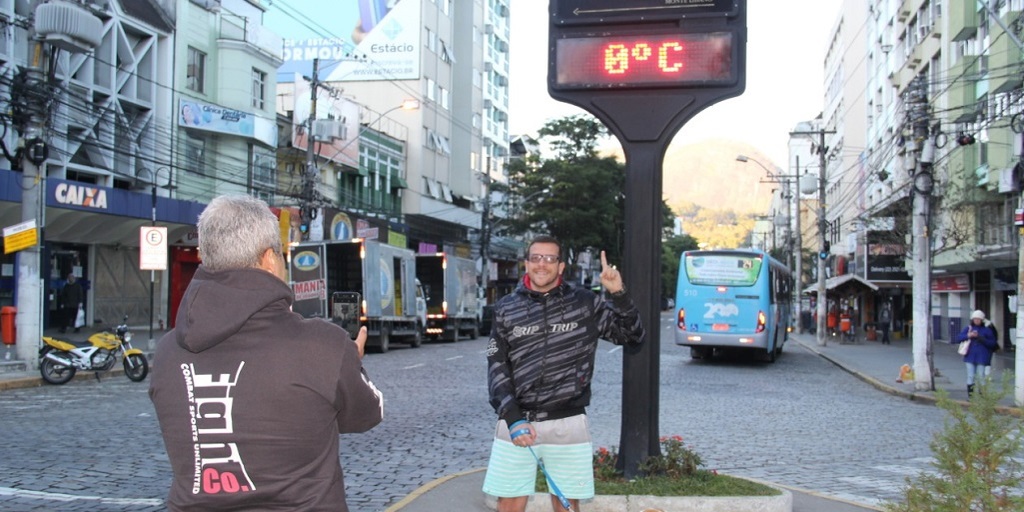 Homem de bermuda encara frio intenso para tirar foto em frente a termômetro