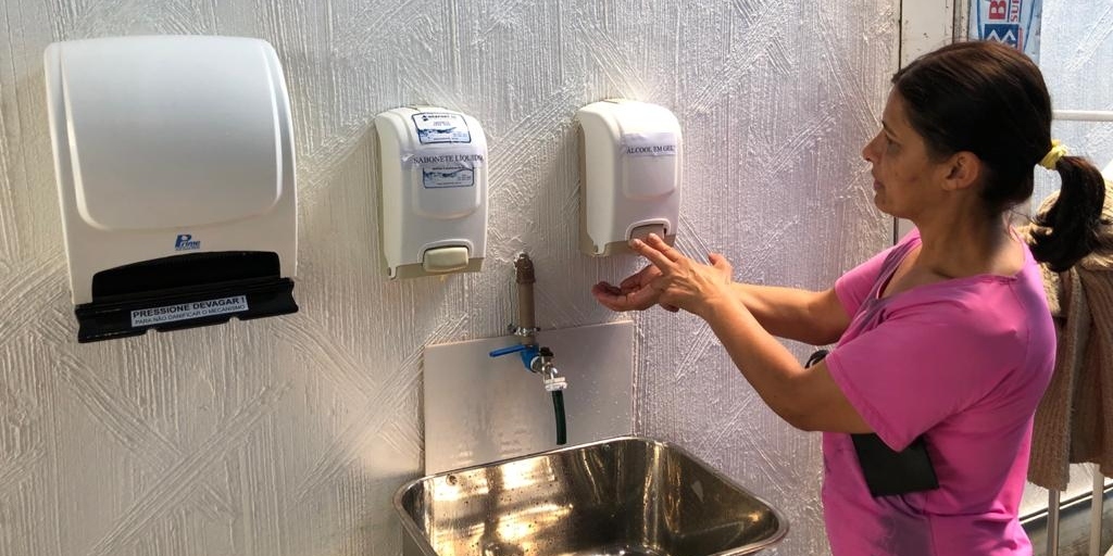 Mulher se higieniza com álcool em gel na porta de um supermercado em Olaria 